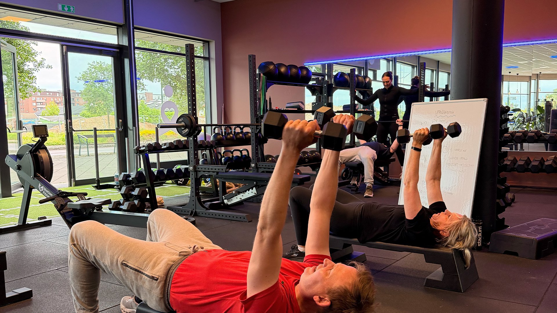 Flera personer tränar styrka med hantlar i ett ljust gym.